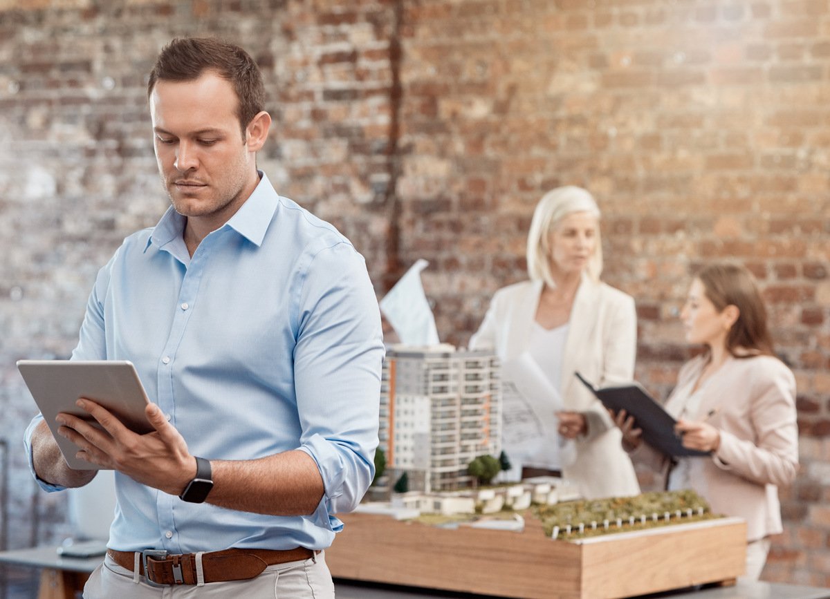 A man looking at a tablet in an office setting next to model buildings