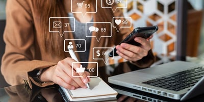 Image of lady holding her phone while in front of her laptop and writing down notes