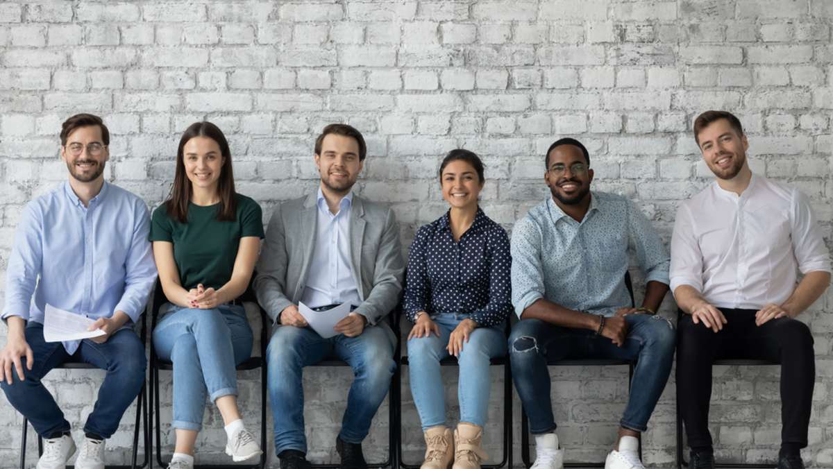 Portrait of smiling diverse multiracial young people sit in row on chairs