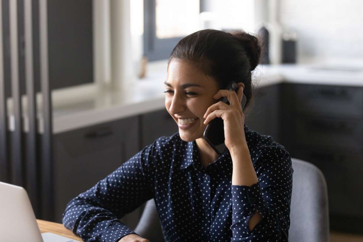 Close up smiling Indian woman talking on phone, laughing, enjoying pleasant conversation with colleague