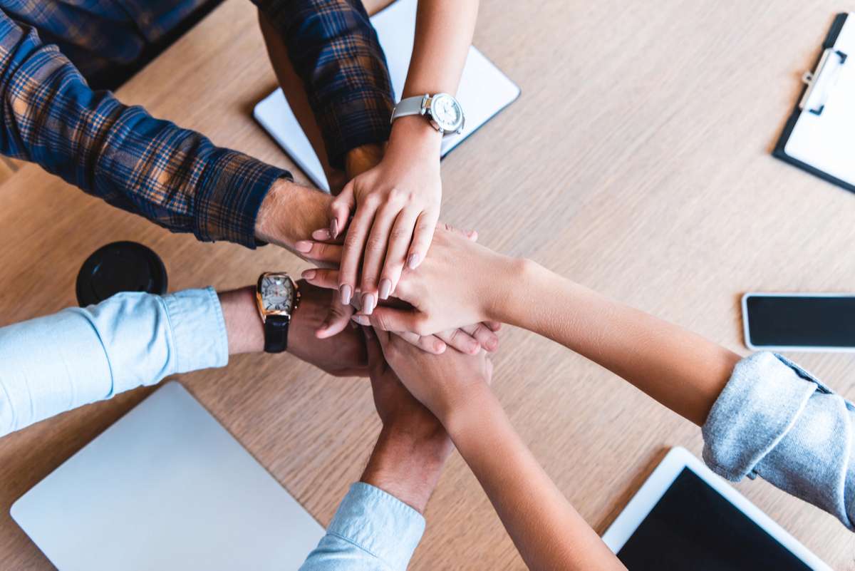 Partial top view of young business colleagues stacking hands at workplace