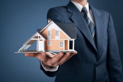 Person wearing a suite holding a scale model of a house 