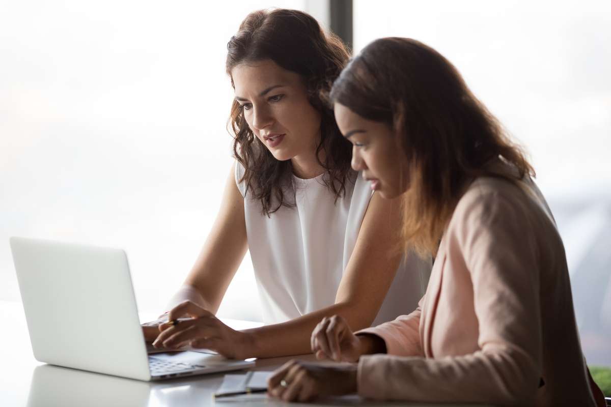 Serious diverse businesswomen discussing online project together looking at laptop