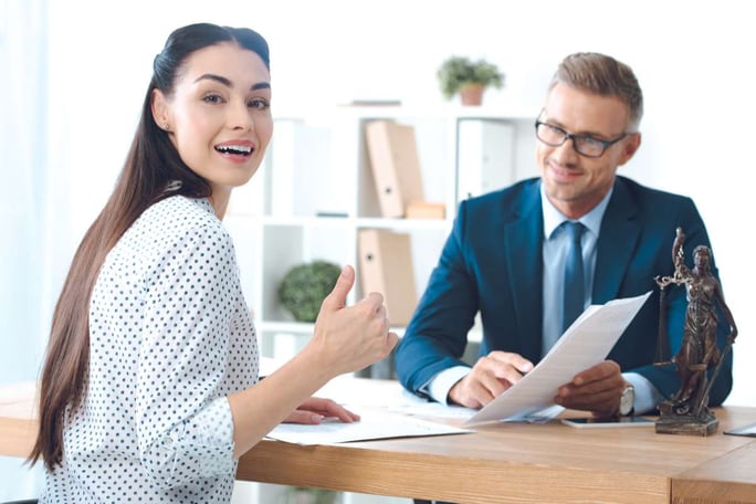 Smiling lawyer holding papers and happy client showing thumb up and looking at camera