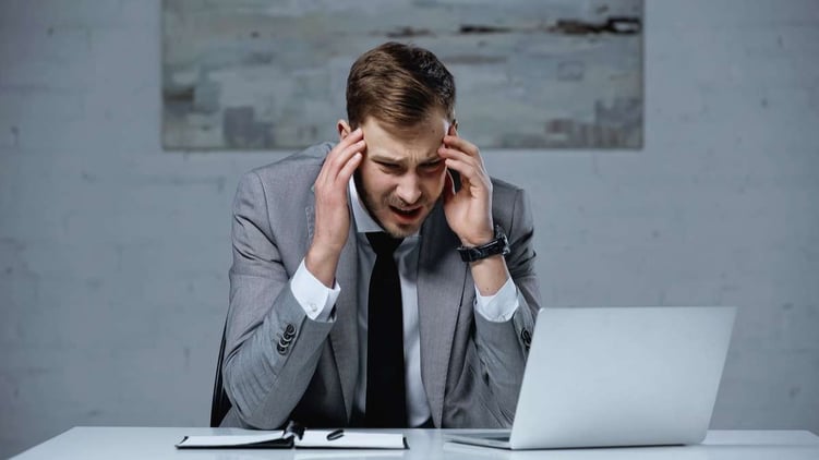 Upset businessman in suit touching head while having migraine in office
