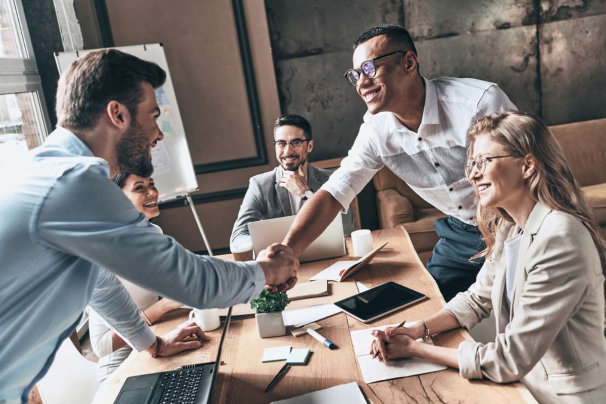 Welcome to our team! Top view of young modern men in smart casual wear shaking hands while working in the creative office