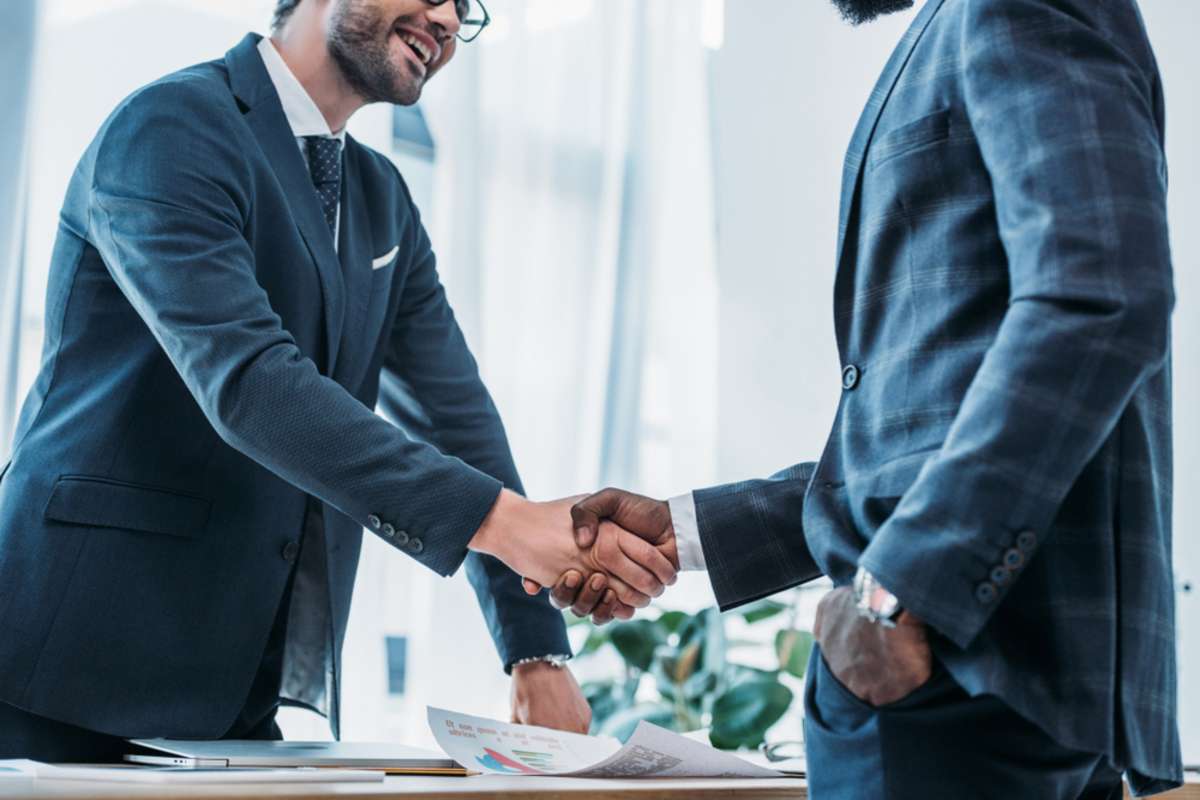 Smiling businessmen shaking hands in office, growing property management company concept. 