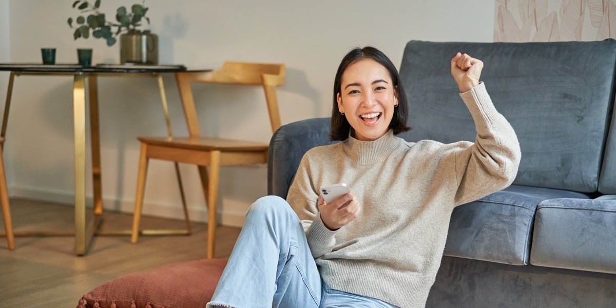 A happy person sitting on the ground in their home holding their phone