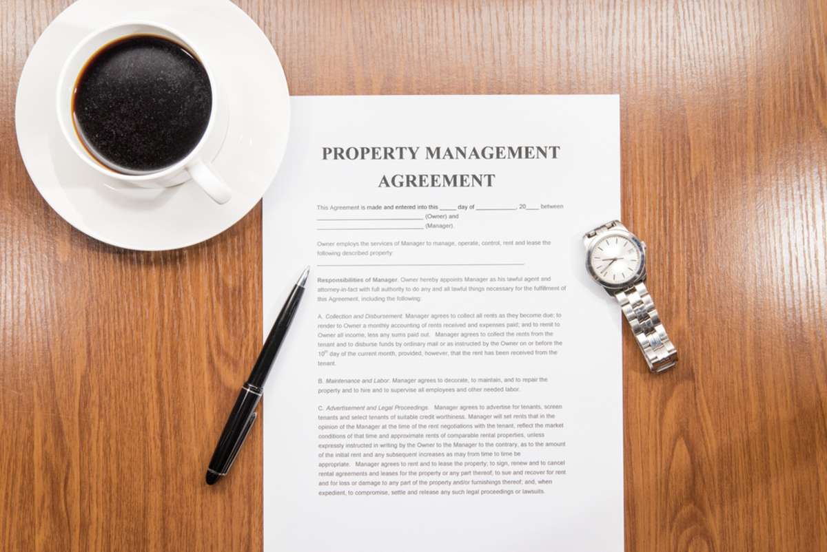 Property management agreement documents on top of a desk with a cup of coffee and a watch beside it