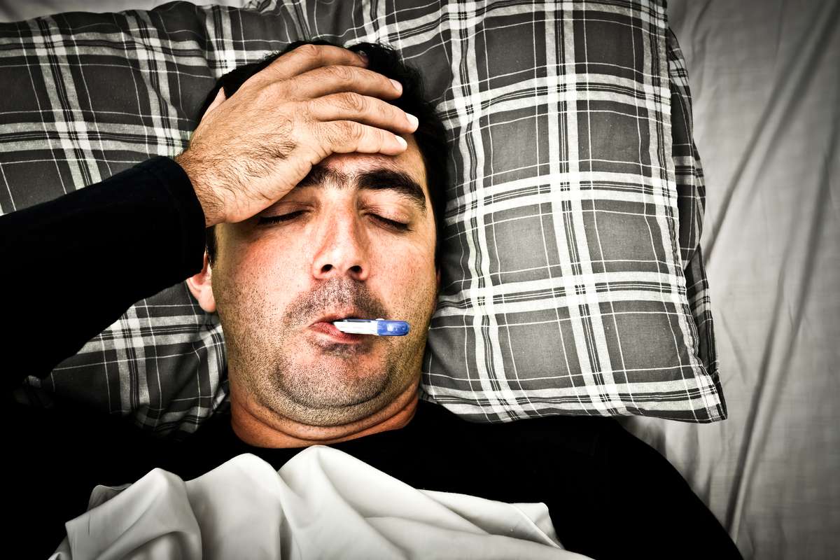 Man laying down on bed sick with a thermometer in his mouth