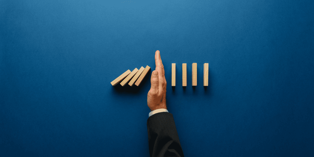 09 Top view of businessman hand stopping falling dominos in a business crisis management conceptual image