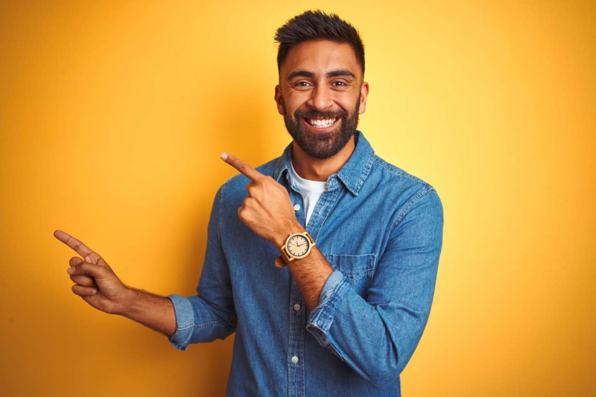 Young man in front of a solid yellow backdrop pointing upward 